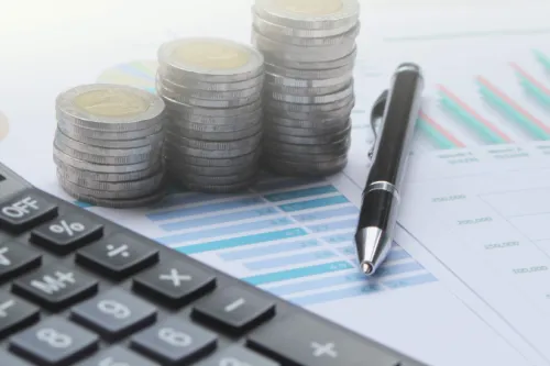 Calculadora, pilhas de moedas e uma caneta sobre gráficos financeiros